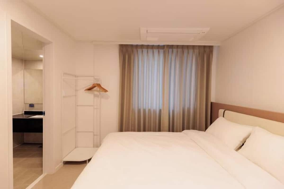 Une chambre d’hôtel avec un lit, une armoire, un miroir et une fenêtre avec des rideaux.