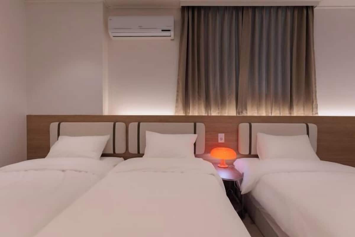 Une chambre d’hôtel avec deux lits, un appareil de climatisation, une fenêtre avec des rideaux et une lampe de chevet.