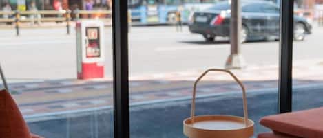A window view of a street with a bus and cars, a bus stop, and a wooden chair.