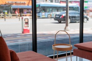 A window view of a street with a bus and cars, a bus stop, and a wooden chair. - WECO STAY Cheongnyangni (Seoul)