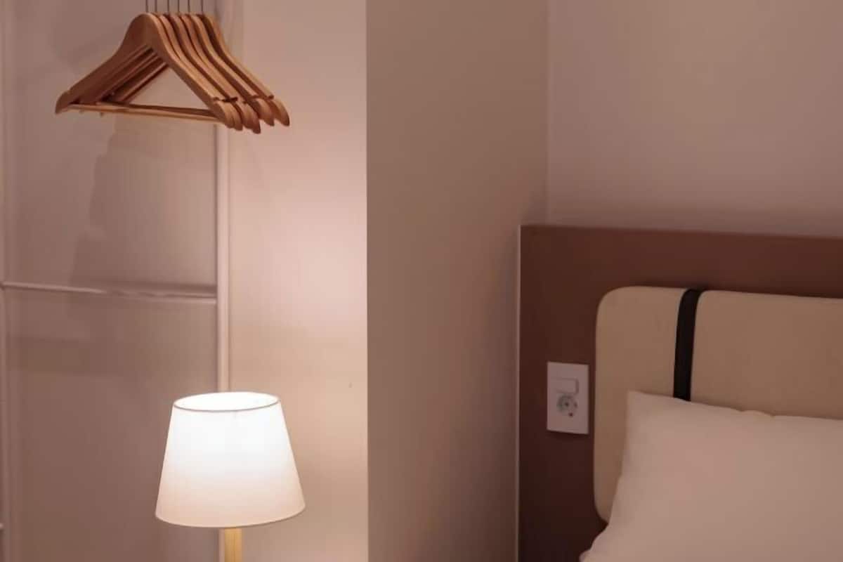 Une chambre d’hôtel avec un lit, une lampe de chevet, un cintre en bois et une prise électrique au mur.