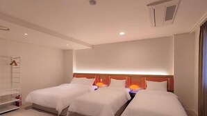 Ein Hotelzimmer mit zwei Betten, einem Kleiderschrank, einem Deckenlüfter und einem Nachttisch mit einer Lampe.