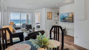 Un soggiorno moderno con vista sull'oceano, un'area pranzo con tavolo rotondo e una TV a parete.