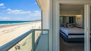 Un balcone con vista sulla spiaggia, una camera da letto con un letto e comodini, e una porta che dà sulla spiaggia.