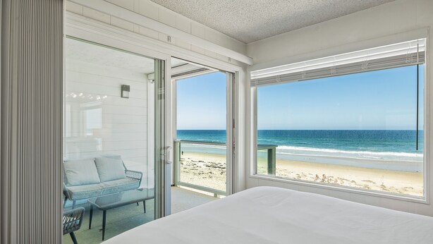 Una camera d'albergo con un letto e una porta vetrata che dà su un balcone con vista sulla spiaggia.