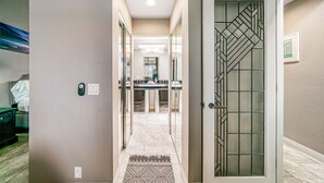 A hallway with a patterned rug, a door with a geometric glass design, and a kitchen area in the background. - Whitewater Village Charm - 30 Night Minimum (Oceanside)