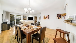 Un comedor con una mesa de madera dispuesta para cuatro personas, rodeada de sillas. Se observa una araña colgante sobre la mesa, y un televisor montado en la pared.