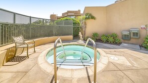 Una piscina en la azotea con una escalera metálica, una silla de descanso y un pequeño jardín con plantas.