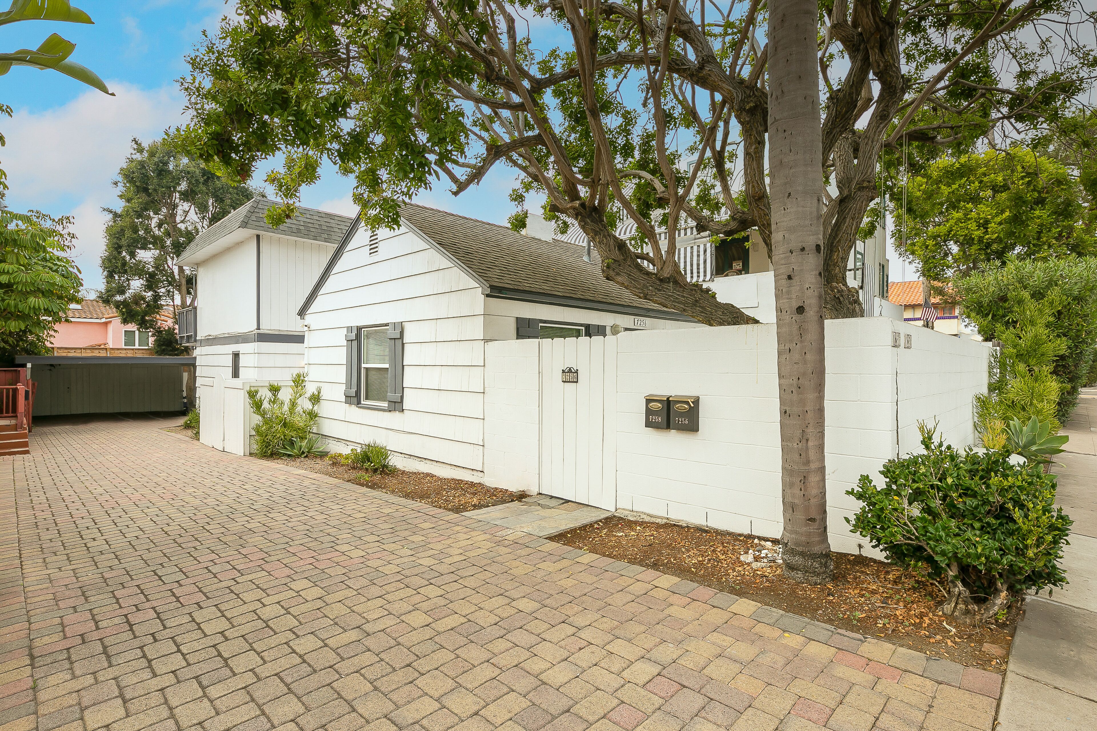 A white two-story house with a brick driveway and a tree in front.