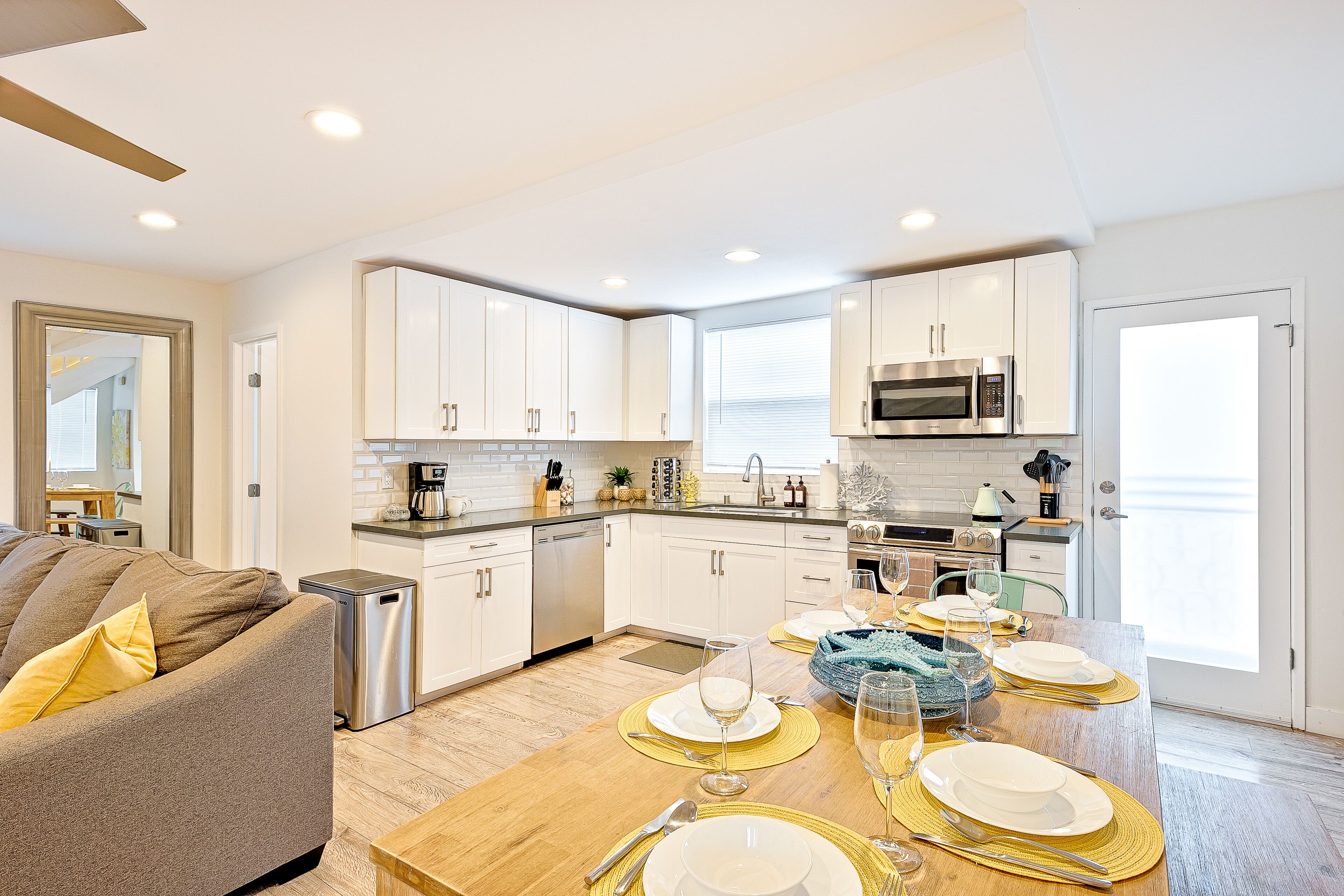 A modern kitchen with white cabinets, stainless steel appliances, and a dining area set for six with gold placemats and white plates.