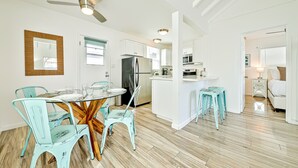 Una cocina moderna con armarios blancos, un refrigerador de acero inoxidable y un comedor con sillas turquesa y una mesa de vidrio.