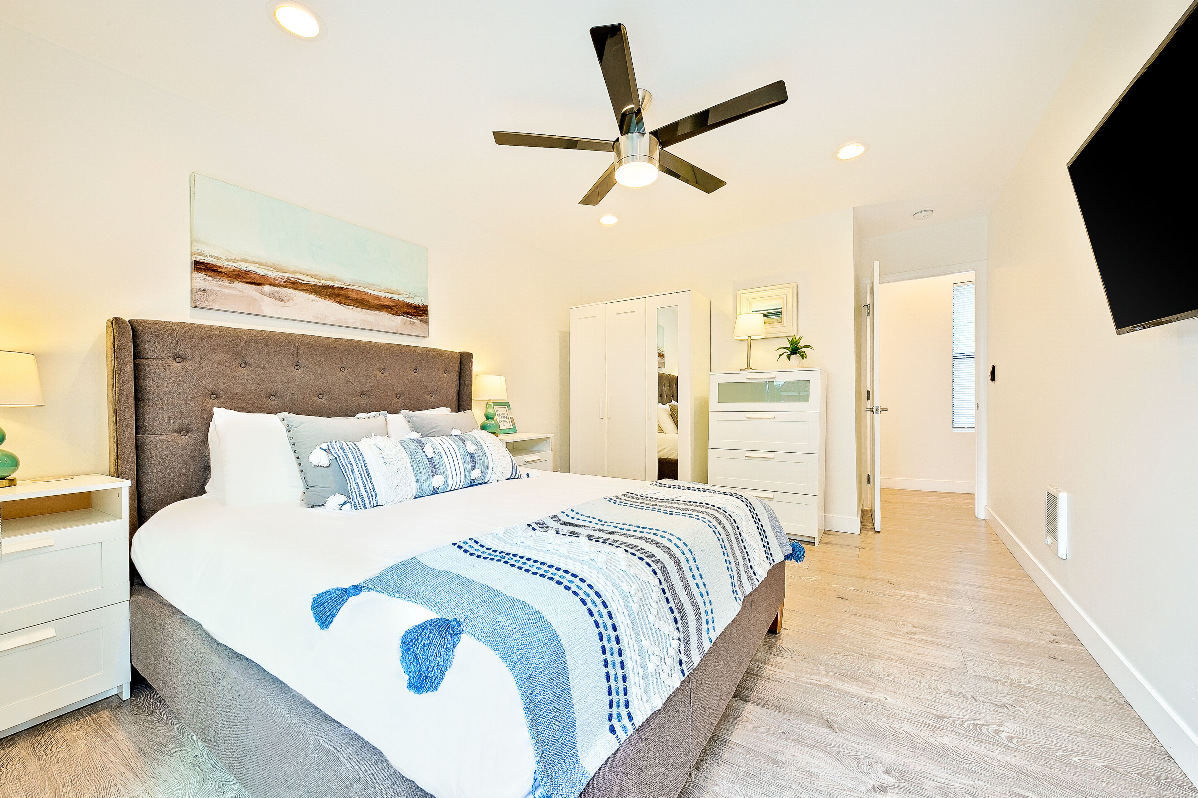 Une chambre moderne avec un grand lit, un ventilateur de plafond et un téléviseur à écran plat fixé au mur.