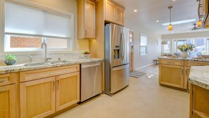 Una cocina moderna con armarios de madera, electrodomésticos de acero inoxidable y un amplio ventanal con persianas.