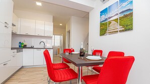 Une cuisine moderne avec des meubles blancs, un plan de travail en bois et un coin repas avec des chaises rouges et une table dressée pour deux personnes.