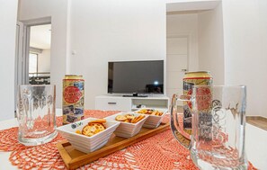 Un saló modern amb un televisor de pantalla plana, una taula de centre de vidre amb aperitius i un corredor de taula vermell amb dibuixos.