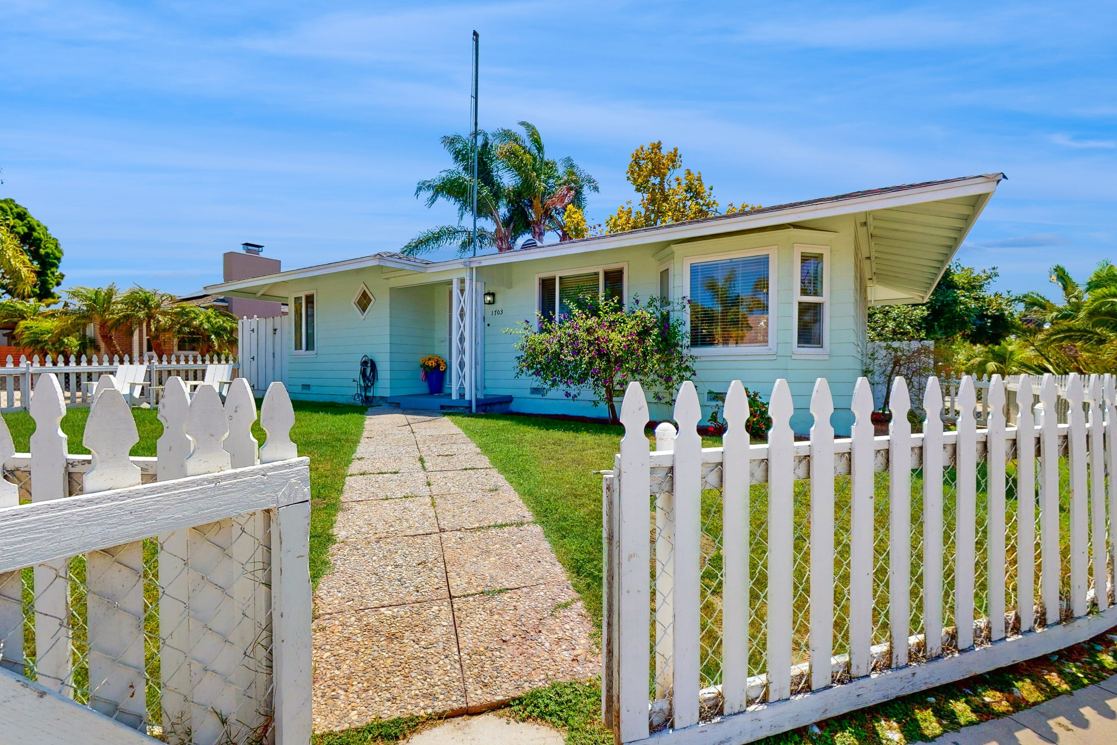 A single-story house with a white picket fence, a front porch, and a small garden.