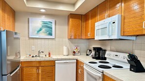 A modern kitchen with wooden cabinets, a stainless steel refrigerator, a microwave, a stove, and a dishwasher.
