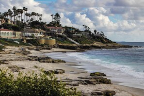 A coastal area with rocky beach, ocean waves, and residential buildings with balconies overlooking the sea.