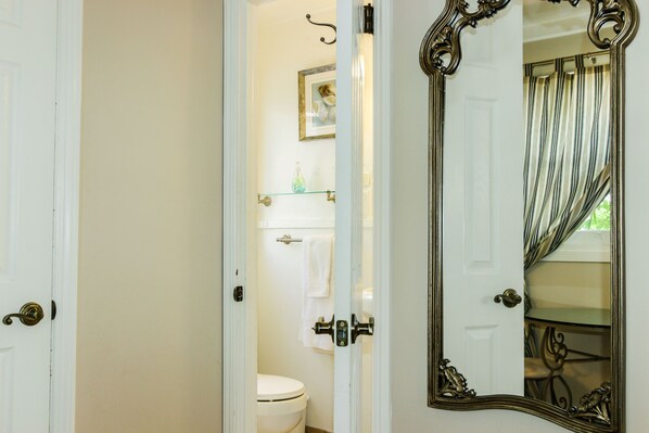 A bathroom with a toilet, a glass shelf, and a mirror.