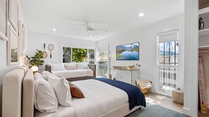 Une chambre moderne avec un grand lit, un petit canapé, une télévision et un balcon offrant une vue sur la mer.
