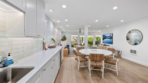 Une cuisine moderne avec des meubles blancs, un évier en acier inoxydable et un coin repas comprenant une table ronde et des chaises.