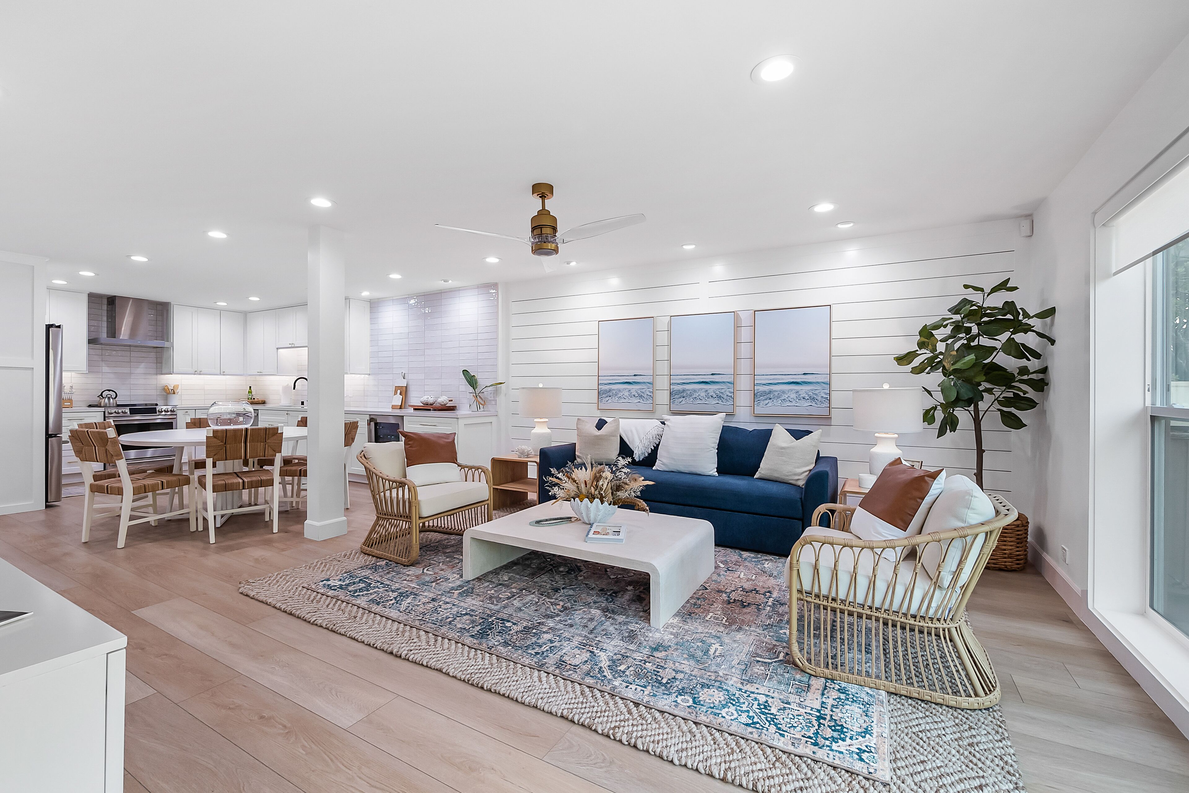 Una sala de estar moderna con una mesa de centro blanca, sofá azul, sillas de mimbre y un ventanal grande.