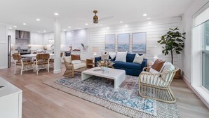 Un salon moderne avec une table basse blanche, un canapé bleu, des fauteuils en osier et une grande fenêtre.