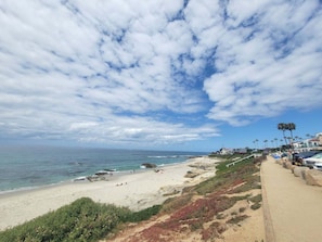 A coastal beach with a sandy shore, a clear sky, and a pathway leading to a building with palm trees. - Playa Del Sur Getaway La Jolla (La Jolla)