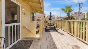 A wooden deck with a picnic table and chairs, a covered area with a door marked "718", and a view of neighboring buildings. - Sweet Sunset Studio Charming Condo (San Diego)