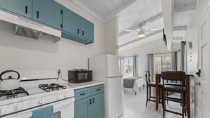 A modern kitchen with a gas stove, microwave, and refrigerator. There is a dining area with a table and chairs. - Sweet Sunset Studio Charming Condo (San Diego)