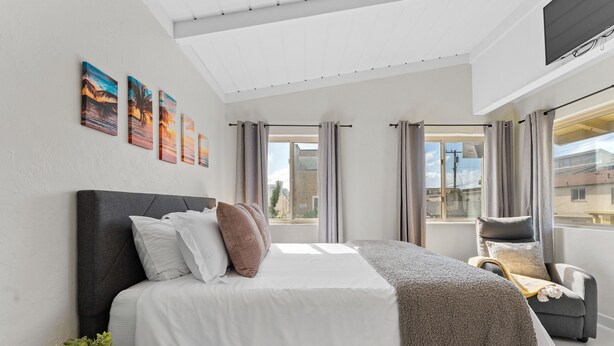 A modern bedroom with a large bed, a chair, and a view of the city. - Sweet Sunset Studio Charming Condo (San Diego)