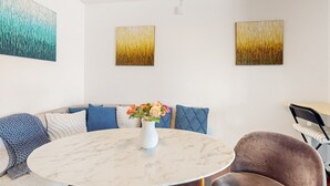 Ein modernes Wohnzimmer mit einem Marmortisch, einer Couch mit gemusterten Kissen und zwei abstrakten Bildern an der Wand.