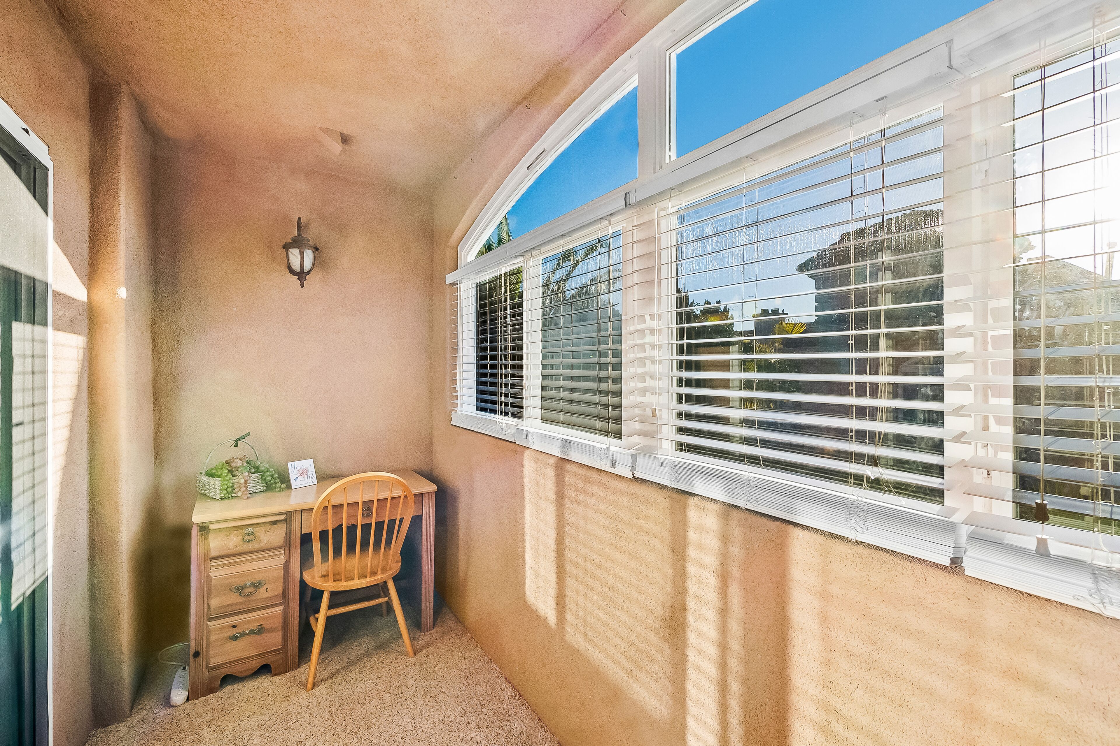 A corner room with a desk, chair, and a window with blinds.