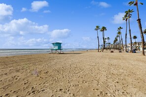 A beach with footprints, a lifeguard tower, palm trees, and ocean waves. - Sandcastle Cottage 22 (Oceanside)