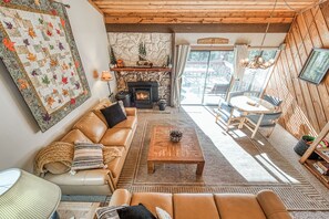 Un salon chaleureux avec une cheminée, un canapé en cuir, une table basse et une vue sur l’extérieur.