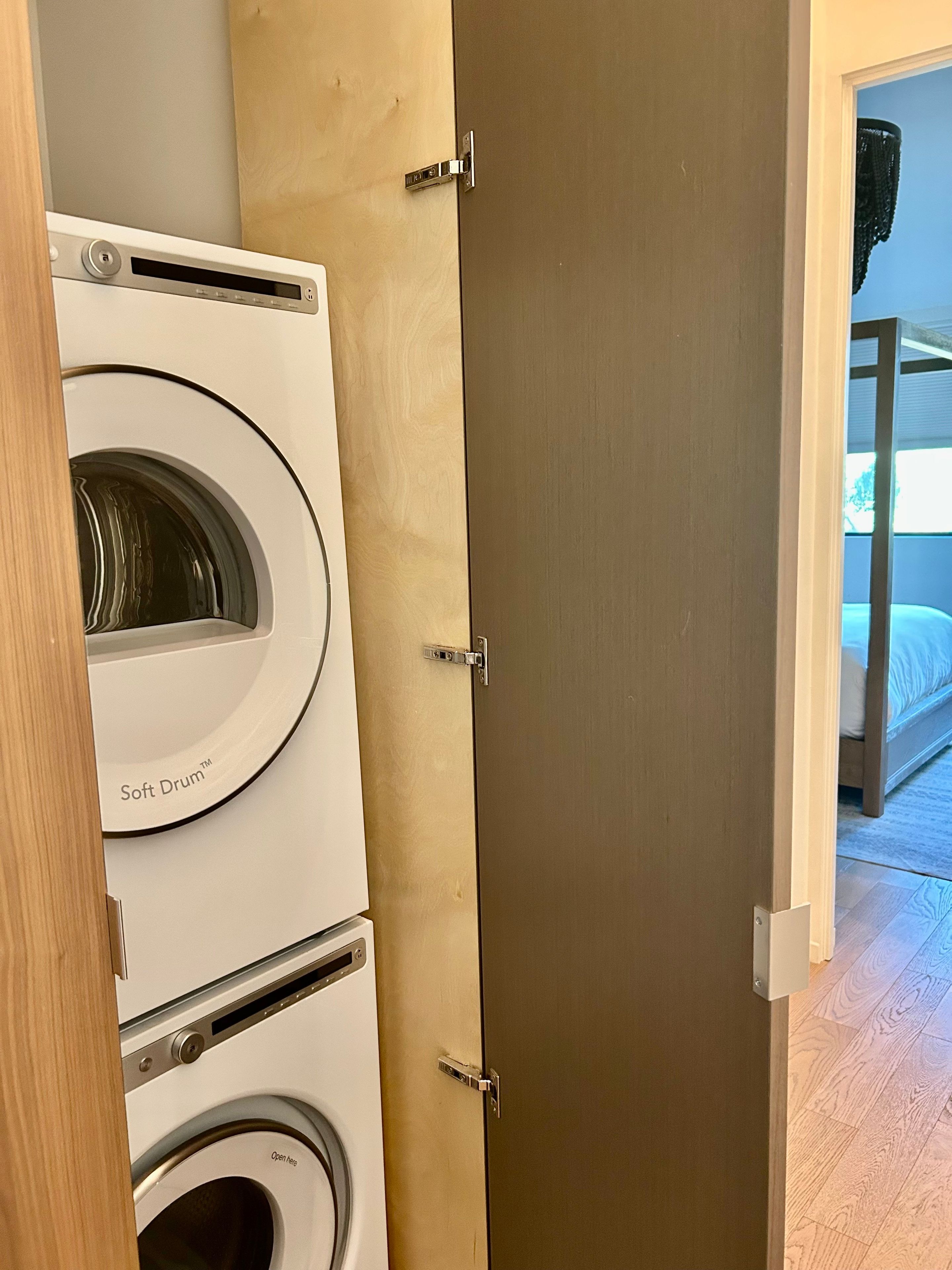 A laundry room with two stacked washing machines and a door leading to a bedroom with a bunk bed.