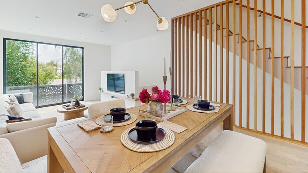 Uma área de refeições moderna com uma mesa de madeira, pratos pretos e brancos e um vaso de flores cor-de-rosa.