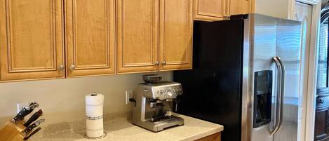 A kitchen with wooden cabinets, a black refrigerator, a coffee maker, and a knife block.