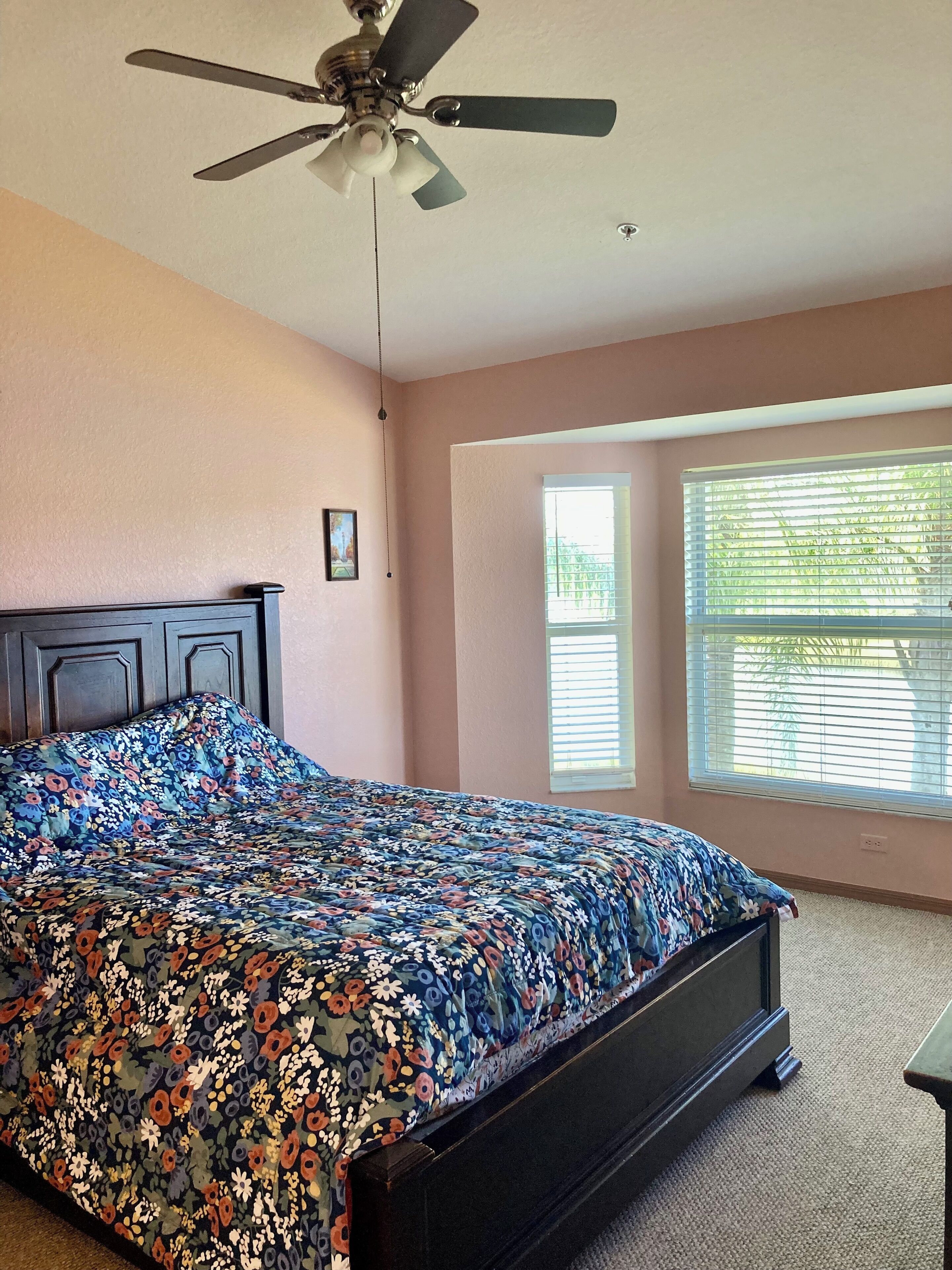 A bedroom with a bed, a ceiling fan, and a window with blinds.