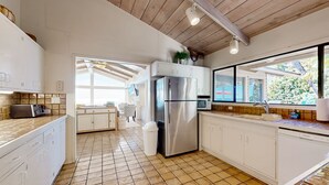 A modern kitchen with white cabinetry, a stainless steel refrigerator, and a tiled floor. - Forever Views Oceanfront (La Jolla)