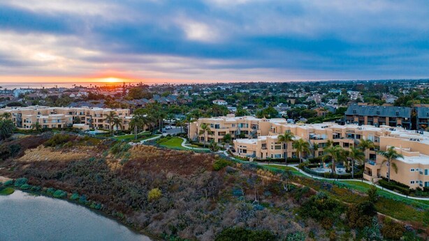 Un quartier résidentiel comprenant plusieurs immeubles d’appartements, un plan d’eau et un coucher de soleil en arrière-plan.