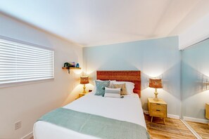 A bedroom with a bed, bedside lamps, a nightstand, a mirror, and a window with blinds. - Pacific Street Hideaway Unit 2 (Oceanside)