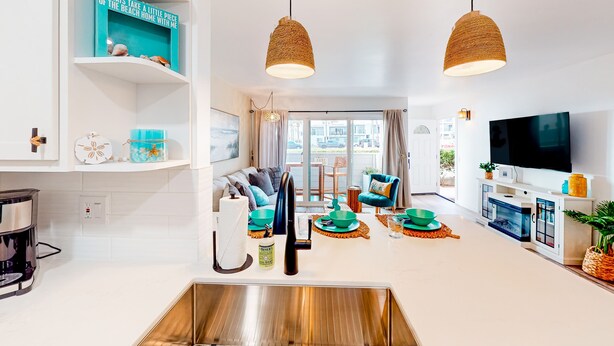 Un soggiorno moderno con angolo cottura, caratterizzato da una grande finestra, una televisione a schermo piatto e un tavolo da pranzo con decorazioni color acquamarina e verde.