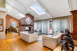 Un salón amplio con chimenea de ladrillo, sofás blancos y un tragaluz grande.