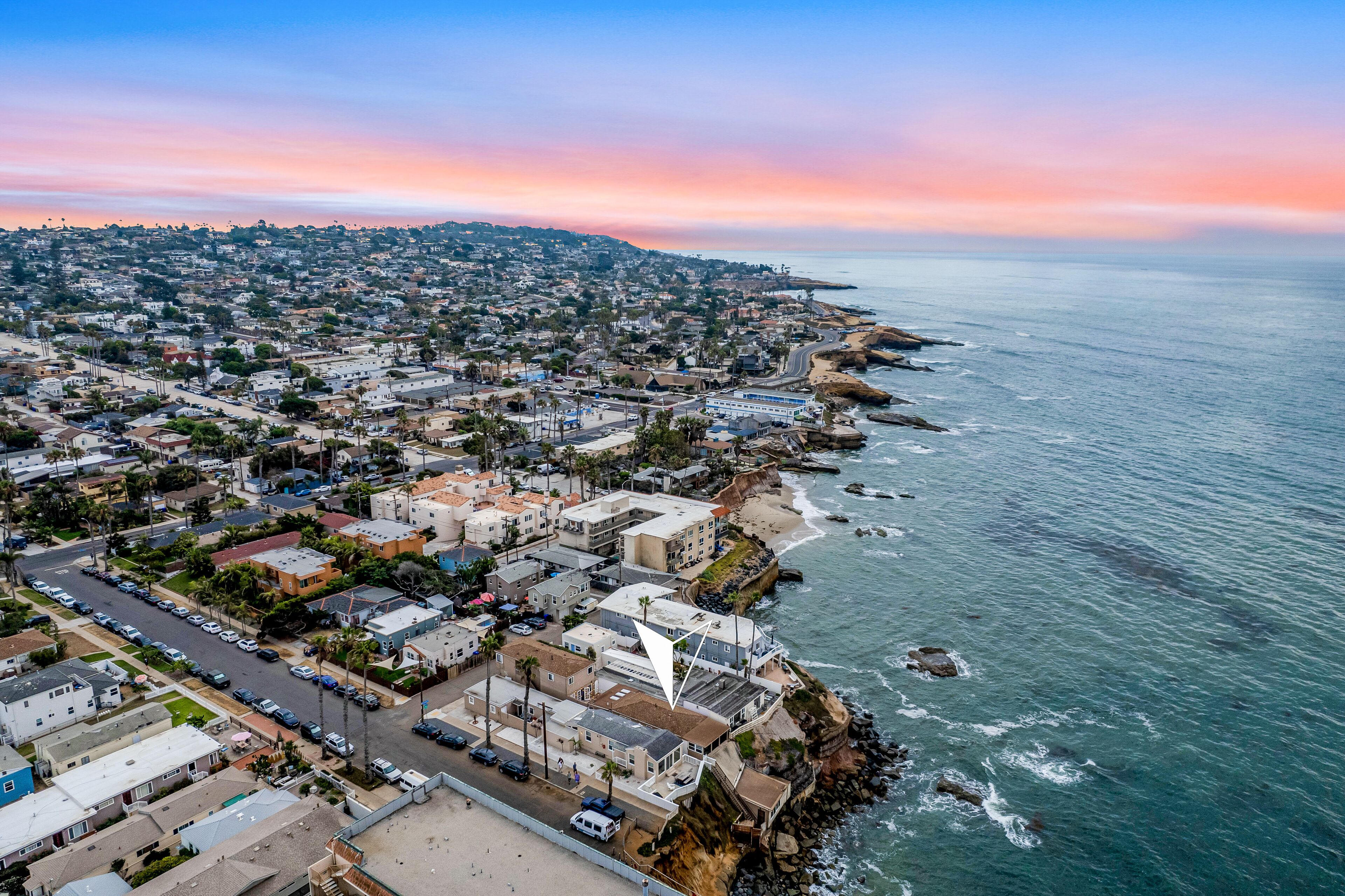 An aerial view of a coastal town with residential buildings, a beach, and a rocky shoreline.