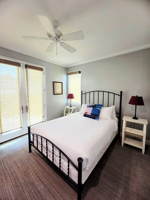 A bedroom with a bed, two bedside tables, a ceiling fan, and a window with a view.