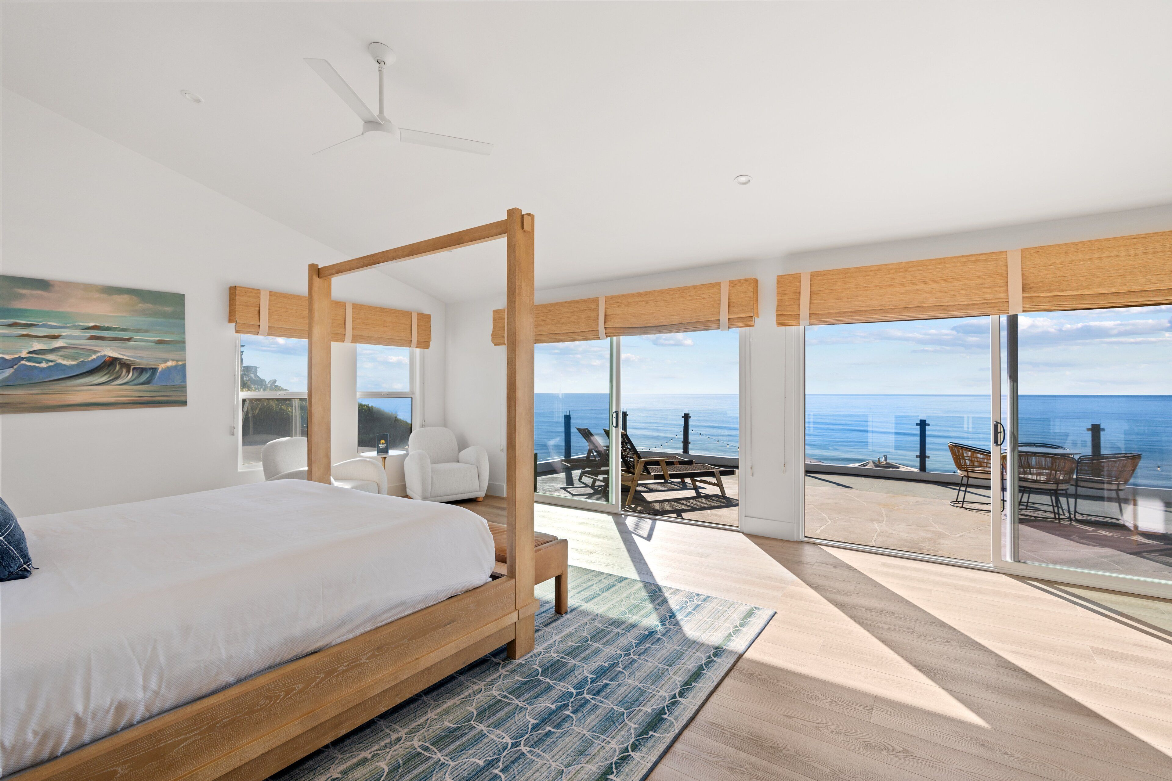 A bedroom with a large bed, a view of the ocean, and a balcony with outdoor furniture.