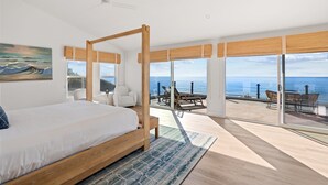 Una camera da letto con un ampio letto, vista sull'oceano e un balcone con mobili da esterno.