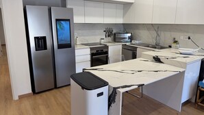 A modern kitchen with white cabinets, a stainless steel refrigerator, a microwave, and a dishwasher.