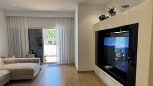 A modern living room with a large TV, a sofa, and a sliding glass door leading to a balcony.
